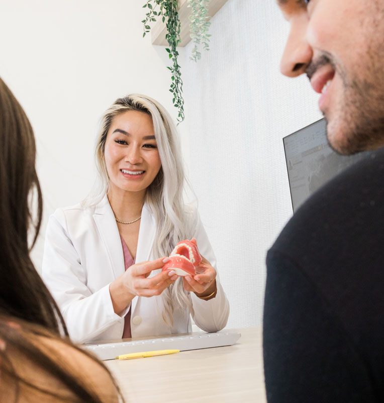 Pediatric dentist demonstrating dental care techniques with a model, engaging with a parent in a welcoming clinic environment at KIND SMILES in Huntington Beach.