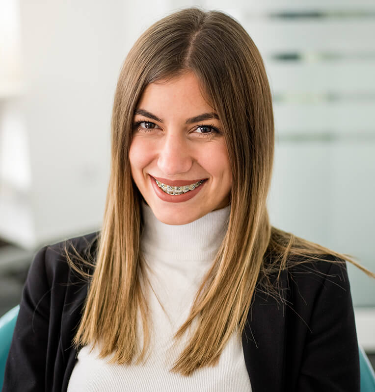 Smiling young woman with braces, showcasing orthodontic treatment options in a modern dental office setting.