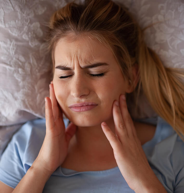 Woman experiencing severe facial pain, indicating potential orthodontic emergency, lying on a bed.