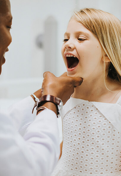 Child smiling with mouth open during pediatric dental exam, receiving gentle care from dentist in a welcoming clinic environment.