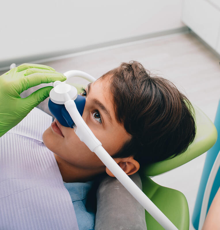 Child receiving nitrous oxide sedation in a pediatric dental office, with a dental professional adjusting the mask, emphasizing comfort and anxiety-free treatment.