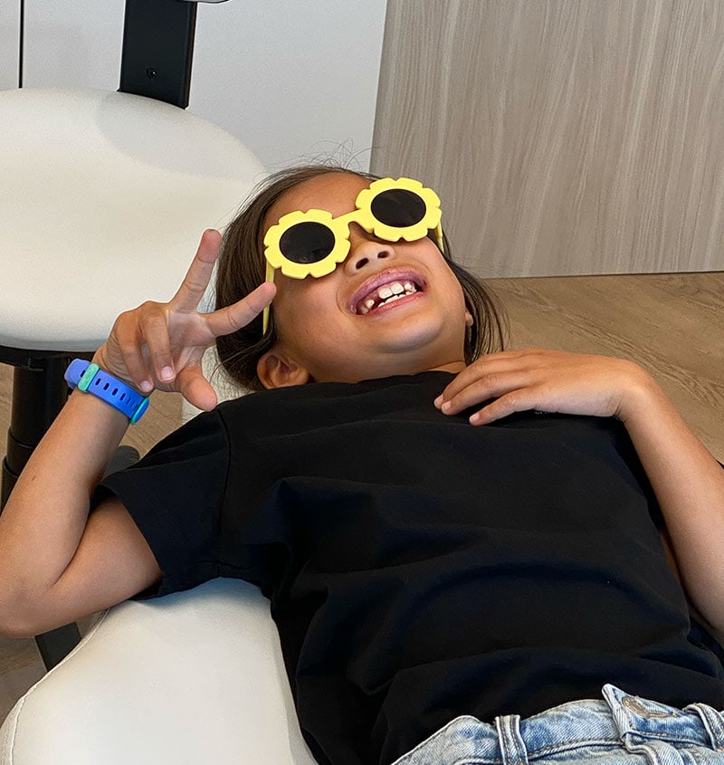 Smiling child with flower sunglasses, illustrating comfortable pediatric dental care at KIND SMILES in Irvine, CA.