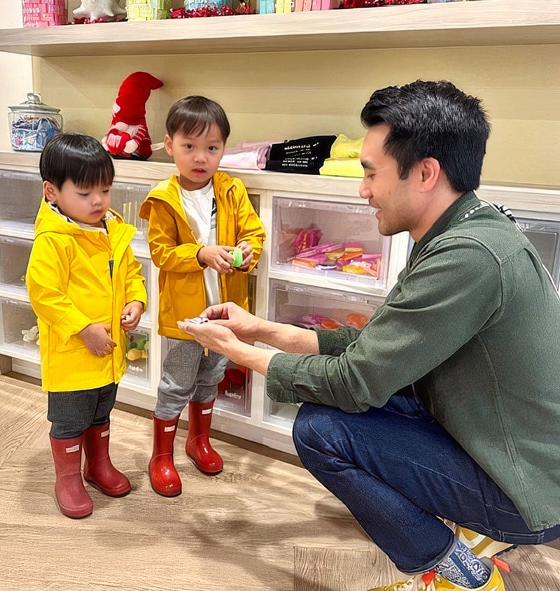 Father smiling with two young children in yellow raincoats, illustrating affordable pediatric dental care in Irvine, CA.