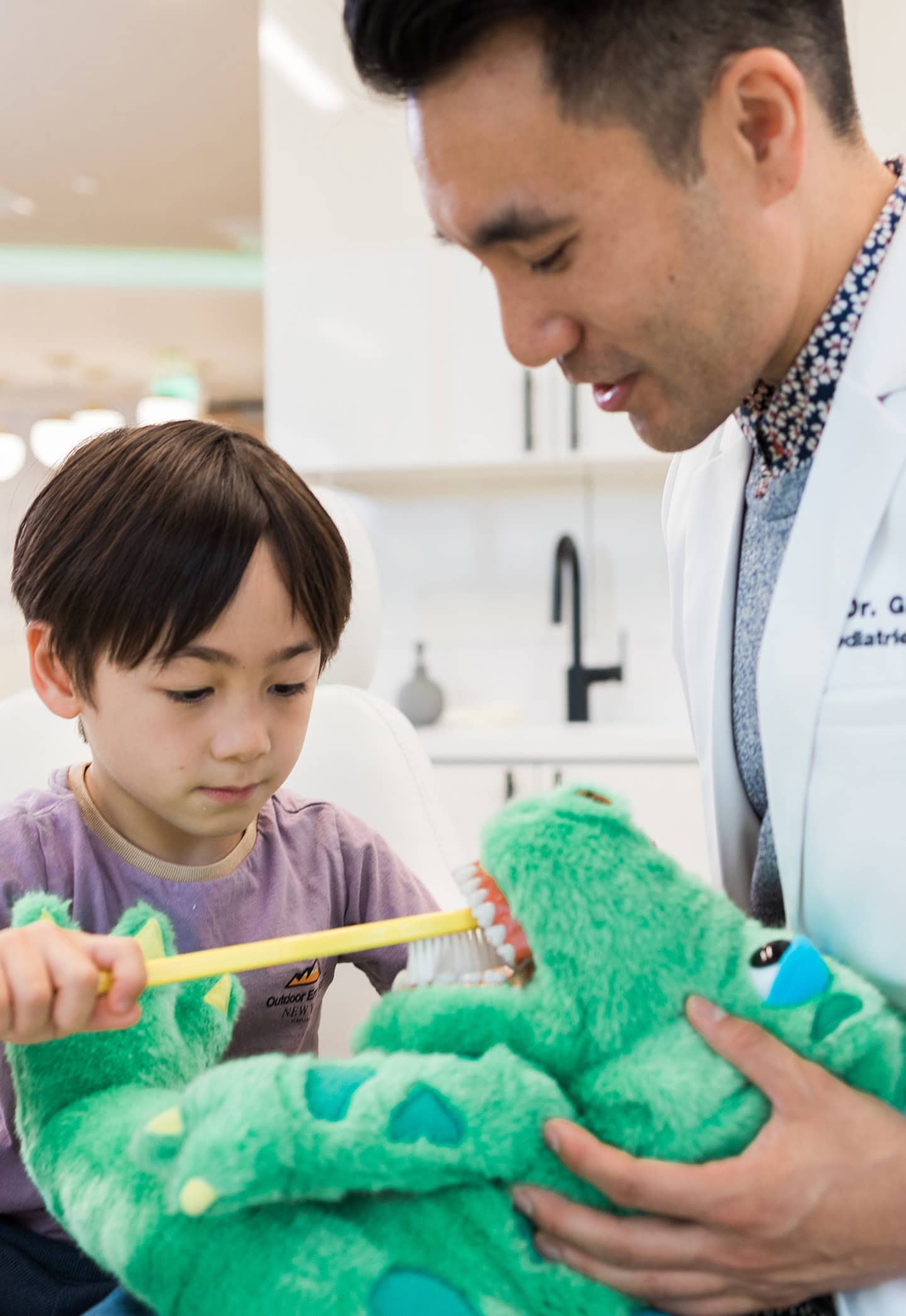 Pediatric dentist examining young patient and demonstrating brushing with a toy crocodile.